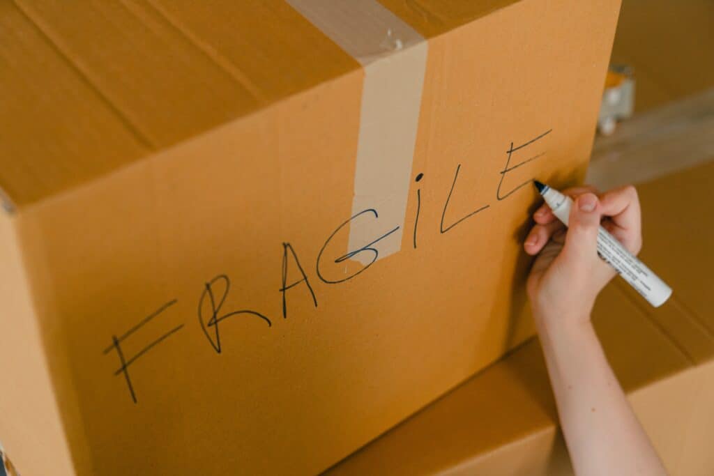 A cardboard box with the hand-written word “FRAGILE” on it, the hand holding the marker still in the picture